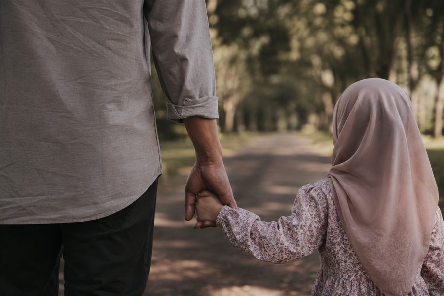 Seorang bapa memegang tangan anak perempuannya semasa berjalan di taman